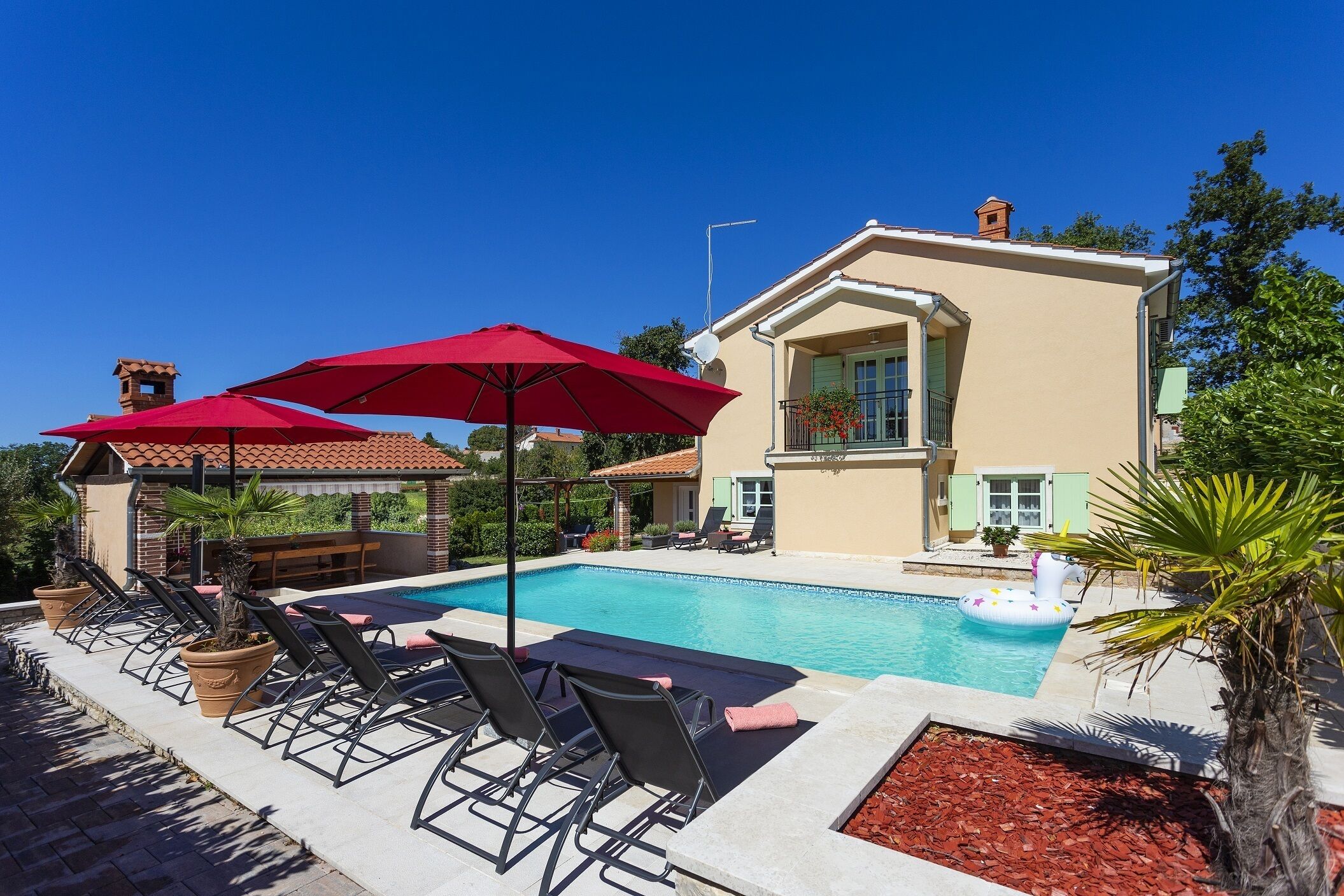 A pool area with lounge chairs and umbrellas, a swimming pool, and a building with a tiled roof.