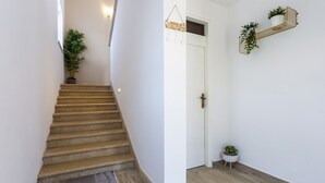 Uma escadaria que leva a uma porta com uma placa de boas-vindas, um vaso de planta no patamar e uma planta pequena no chão.