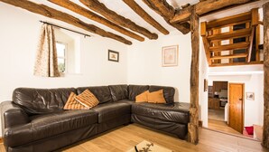 Una sala de estar con un sofá de cuero marrón, vigas de madera en el techo y una escalera de madera que lleva a un nivel superior.