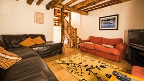 Una sala de estar con un sofá de cuero negro, un sofá rojo, una escalera de madera y un televisor.