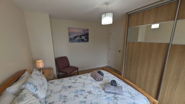 Une chambre à coucher avec un lit, une chaise, une lampe, un tableau et une armoire.