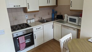 Une cuisine avec des meubles blancs, une cuisinière, un four, un four à micro-ondes et un évier.