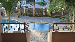 Un espace piscine doté d’une terrasse carrelée en pierre, d’une rambarde en métal et de palmiers.