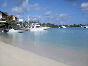 Un port de plaisance où sont amarrés plusieurs yachts, à proximité d’une plage de sable.