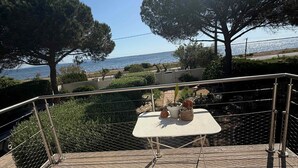 A terrace with metal chairs and a table, overlooking a body of water with trees and a clear sky.