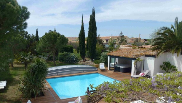 A swimming pool surrounded by greenery, a covered outdoor seating area, and a view of distant buildings.