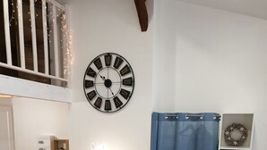 Een moderne woonkamer met een blauwe bank, een grote wandklok, een trap met sfeerverlichting, een blauw gordijn en opbergplanken.