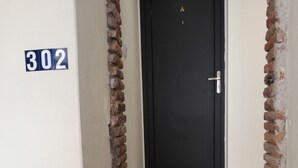 Een zwarte deur met een klein opstapje ervoor, aan weerszijden van bakstenen muren en een witte muur met het nummer 302.