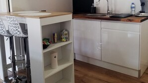 Een compacte keuken met witte kastjes, een magnetron, een spoelbak en een houten plafond.