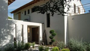 Ein modernes Haus mit einem Kiesweg, der zu einer Holztür führt, umgeben von verschiedenen Pflanzen und Sträuchern.
