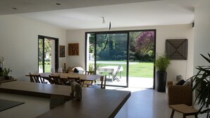 Ein geräumiger Essbereich mit einem großen Tisch, Stühlen und Blick auf einen Garten durch Glastüren.