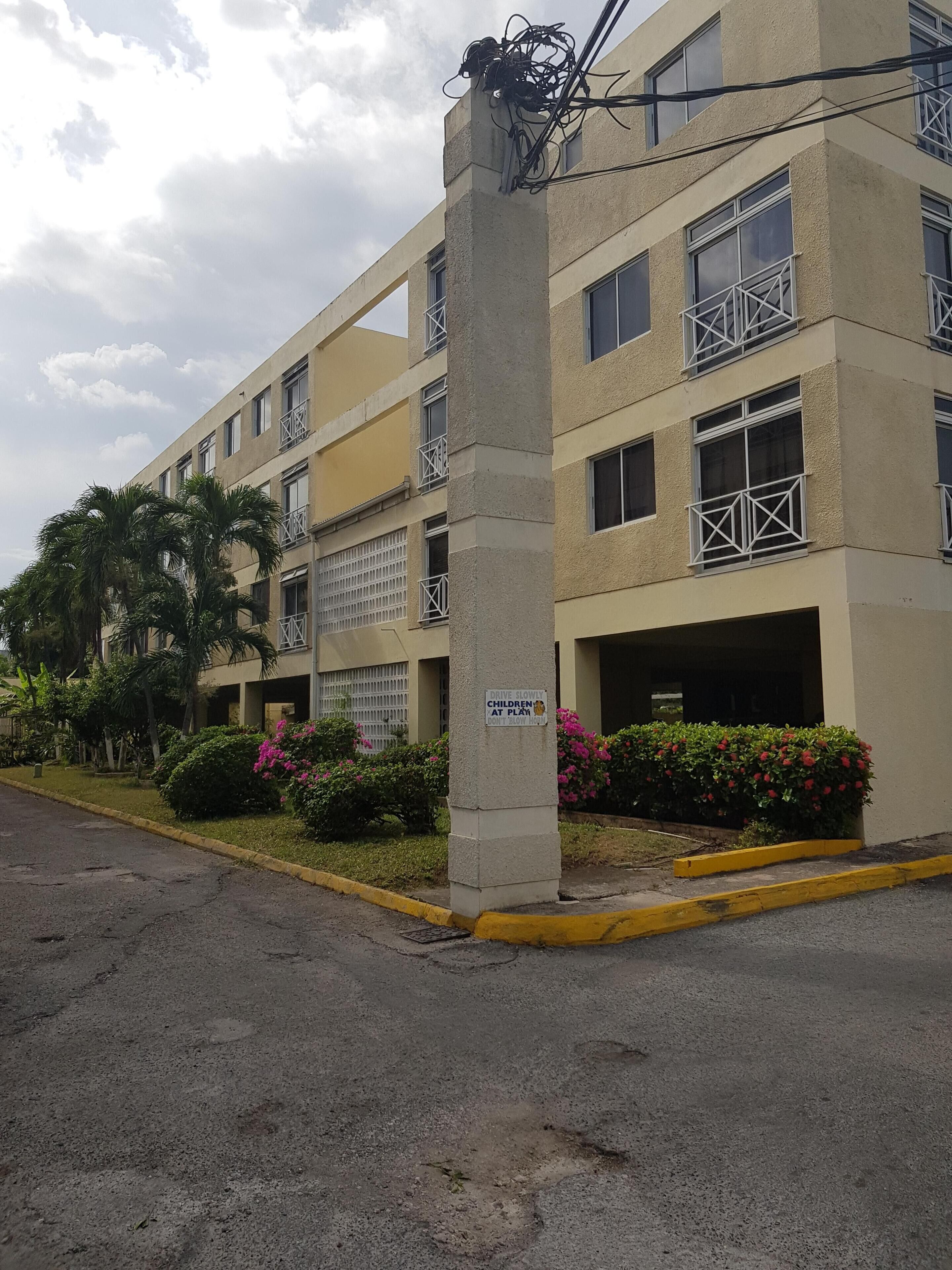 A multi-story building with balconies, a sign advising to drive slowly, and a parking area with yellow curbs.