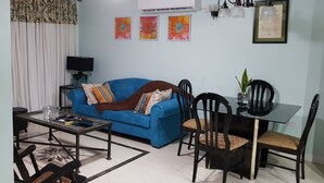 A living room with a blue sofa, dining table, chairs, and a ceiling fan.