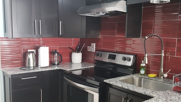 A kitchen with dark cabinets, a stainless steel stove, and a red-tiled backsplash.