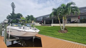 A boat docked at a wooden pier with a house and palm trees in the background. - Villa Alani -- Luxurious south-facing dream villa directly on the canal / river connection (Cape Coral)