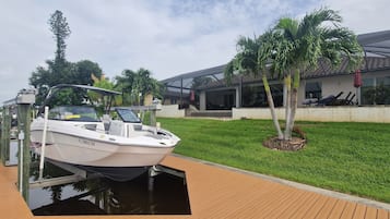 A boat docked at a wooden pier with a house and palm trees in the background.