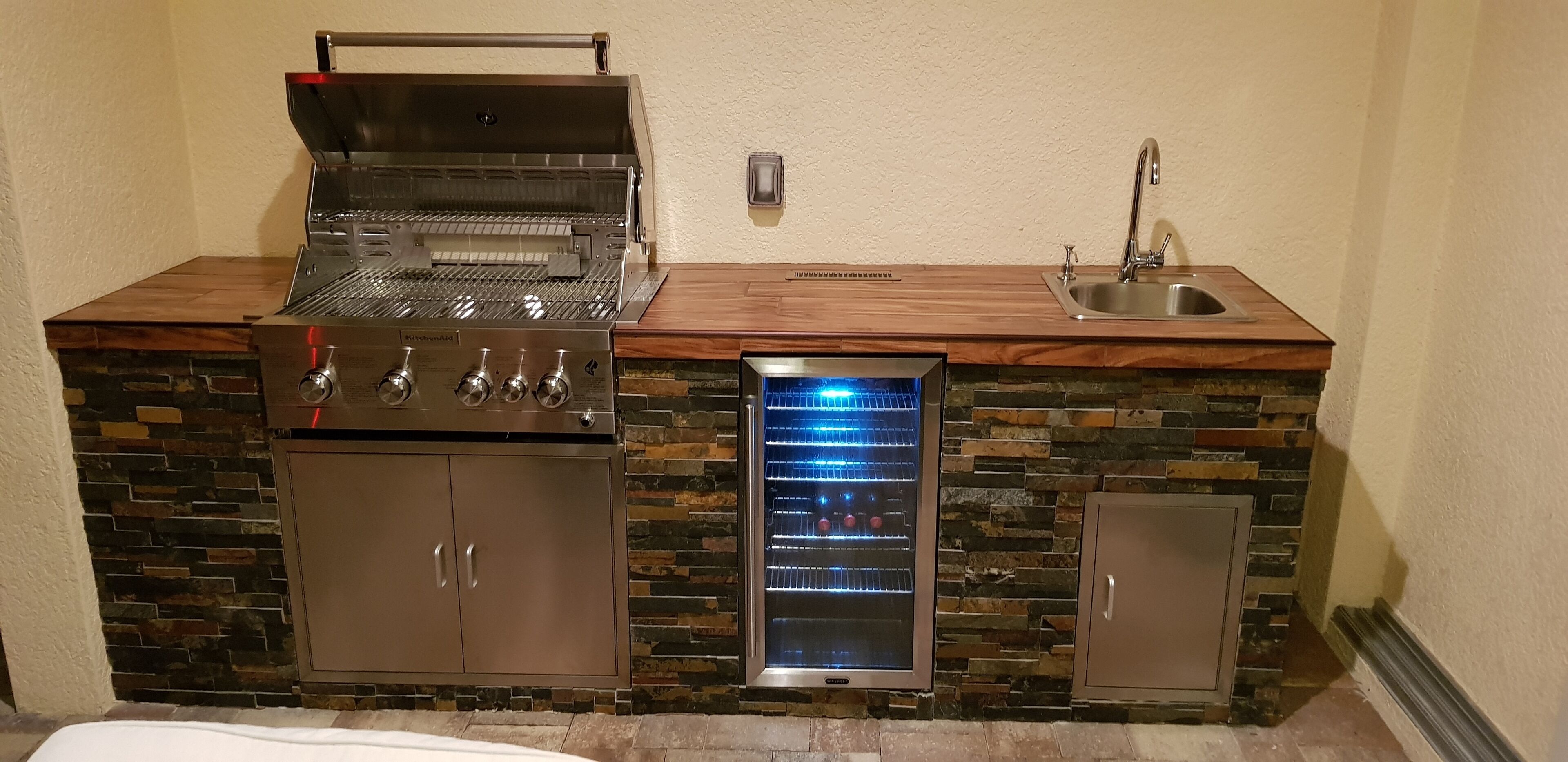 Une cuisine compacte équipée d’un barbecue intégré, d’un réfrigérateur et d’un évier.