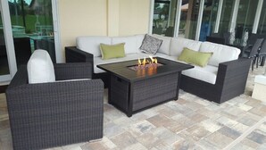 An outdoor seating area with a white sofa, two armchairs, and a coffee table with a built-in fire feature. - Villa Alani -- Luxurious south-facing dream villa directly on the canal / river connection (Cape Coral)