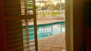Un espace piscine doté d’un patio couvert, de mobilier d’extérieur et offrant une vue sur un jardin aménagé.
