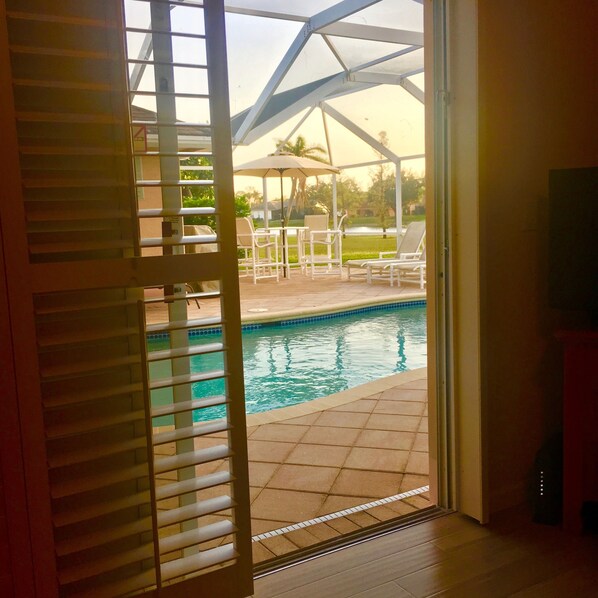 A pool area with a covered patio, outdoor furniture, and a view of a landscaped garden.