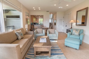 A spacious living room with a sofa, two armchairs, a coffee table, and a dining area in the background.