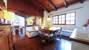 A spacious kitchen with wooden cabinets, a dining area with a wooden table and chairs, and a large window providing natural light. - Garden Villa near Costa Smeralda (Olbia)