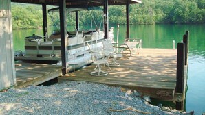A dock with a covered seating area, a boat, and a view of a lake surrounded by greenery. - Cozy Waterfront Cottage -- No Wake Cove, Great Views, New Private Floating Dock (Huddleston)