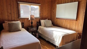 A cabin-style bedroom with two single beds, wooden walls, a nightstand with a lamp, and a window with blinds. - Cozy Waterfront Cottage -- No Wake Cove, Great Views, New Private Floating Dock (Huddleston)
