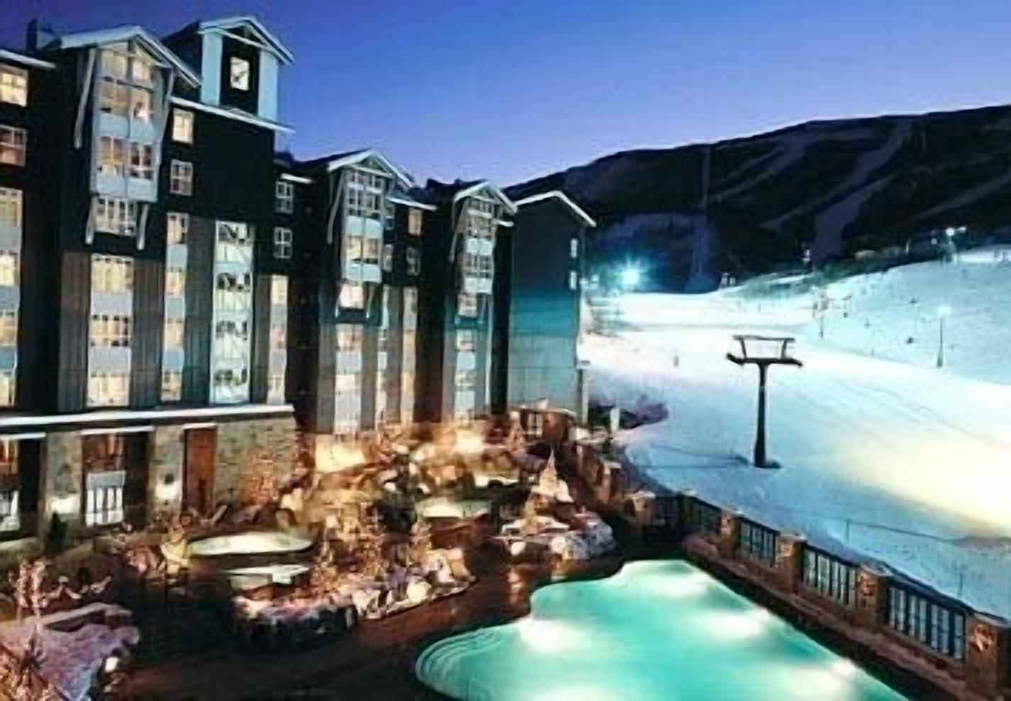 Ein Hotel mit Poolbereich, Sitzgelegenheiten im Freien und Blick auf eine verschneite Landschaft.