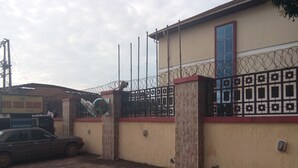 A building with a barbed wire fence, a Heineken sign, and a car parked in front. - Hotel Codial Exclusive (Enugu)
