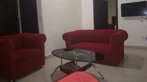 A living room with two red sofas, a glass coffee table, and a flat-screen TV mounted on the wall. - Hotel Codial Exclusive (Enugu)