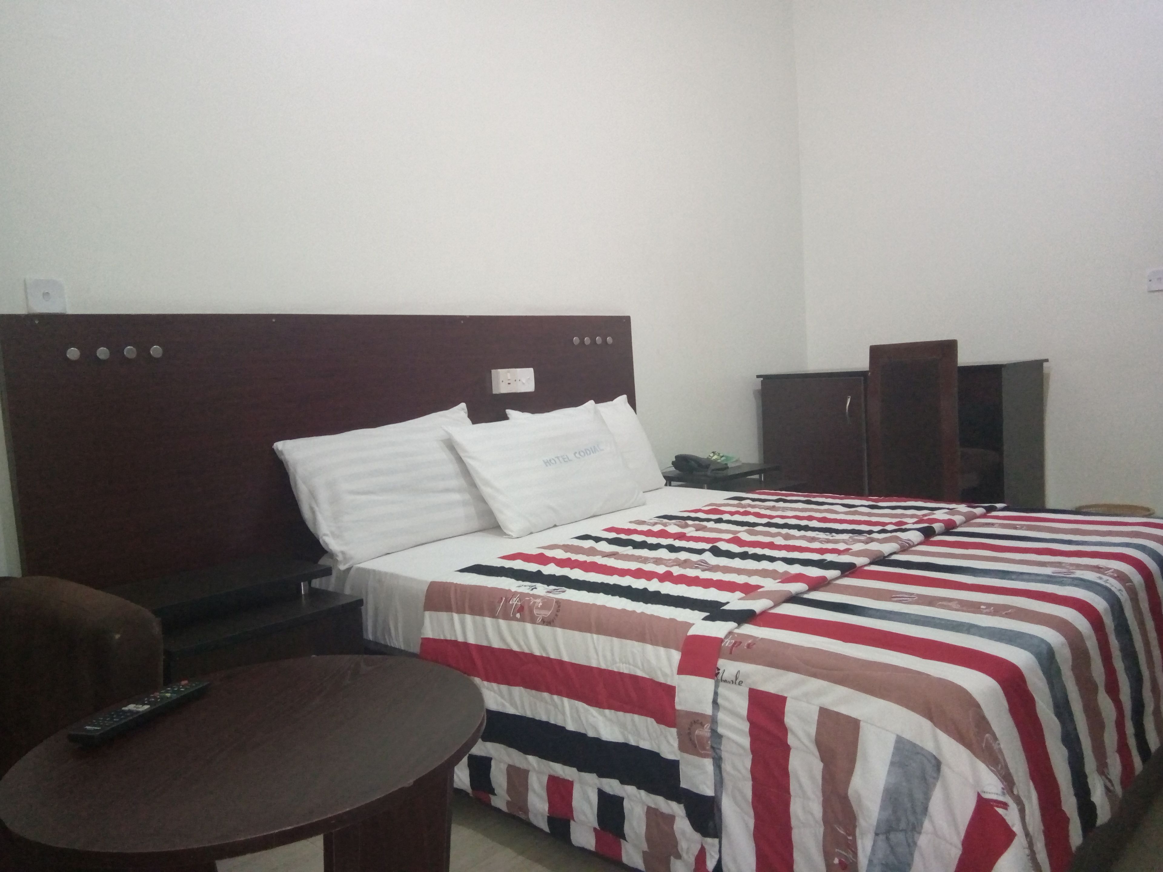 Una habitación de hotel con cama, mesita de noche, una mesa y un armario.