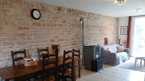 Un salon chaleureux avec un mur en pierre, une cheminée, un canapé et une table à manger avec des chaises.