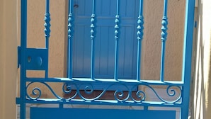 Une porte en métal bleue, ornée de motifs décoratifs, avec une autre porte visible à l’arrière-plan.