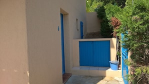 Une ruelle étroite avec une porte bleue et un portail bleu, entourée de verdure.