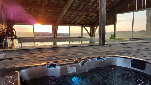 A hot tub with a wooden deck and a view of the sunset over water.