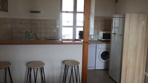 Eine Küche mit Waschmaschine, Mikrowelle und Kühlschrank. Es gibt drei Hocker und einen Holzstuhl.