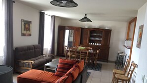 Ein Wohnzimmer mit einer Couch, einem Hocker und einem Essbereich mit Stühlen und einem Tisch.