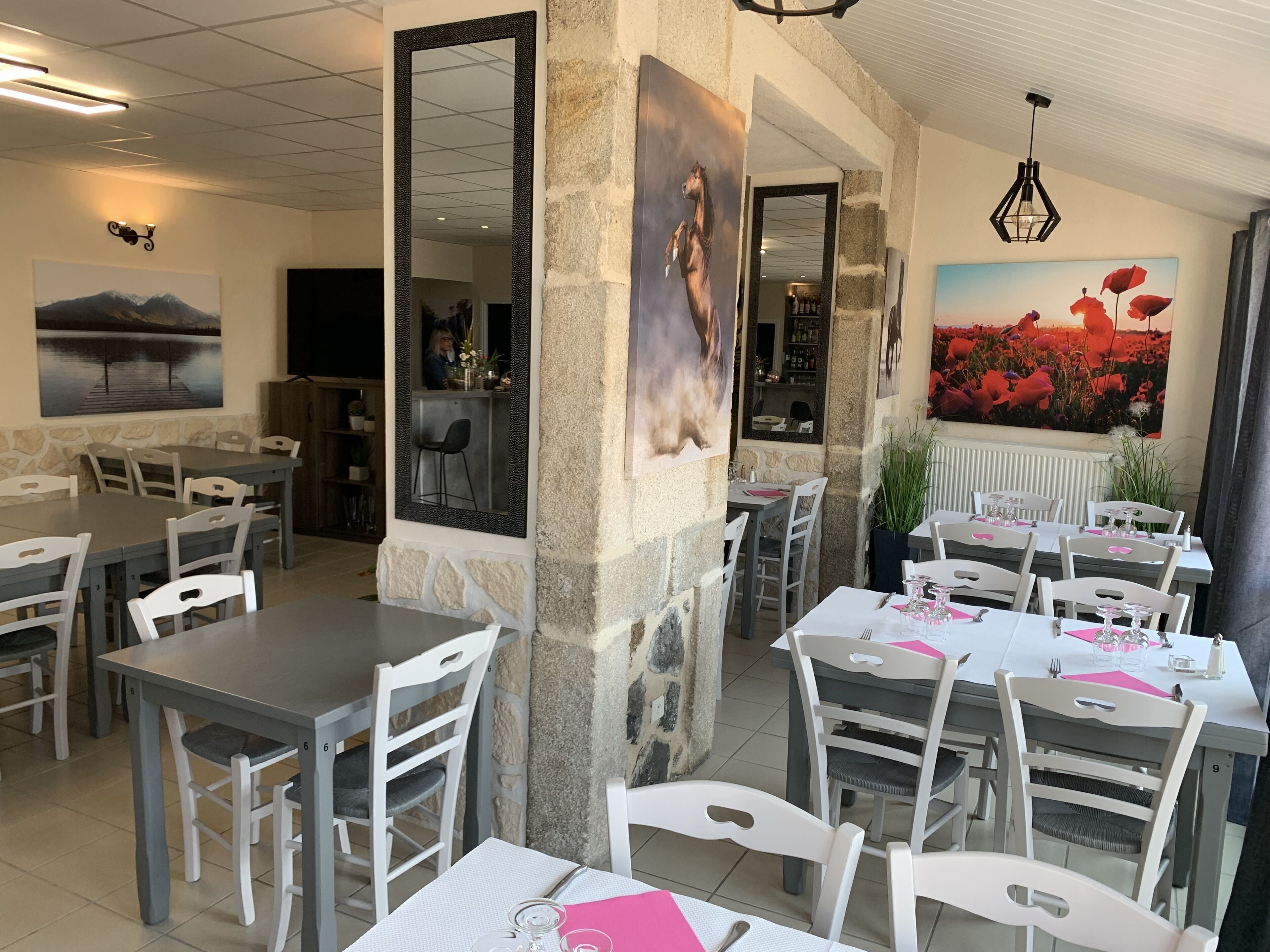 Ein Restaurant mit Steinwänden, weißen und grauen Tischen sowie Stühlen. An den Wänden befinden sich Gemälde und im Hintergrund ist eine Bergblick zu sehen.