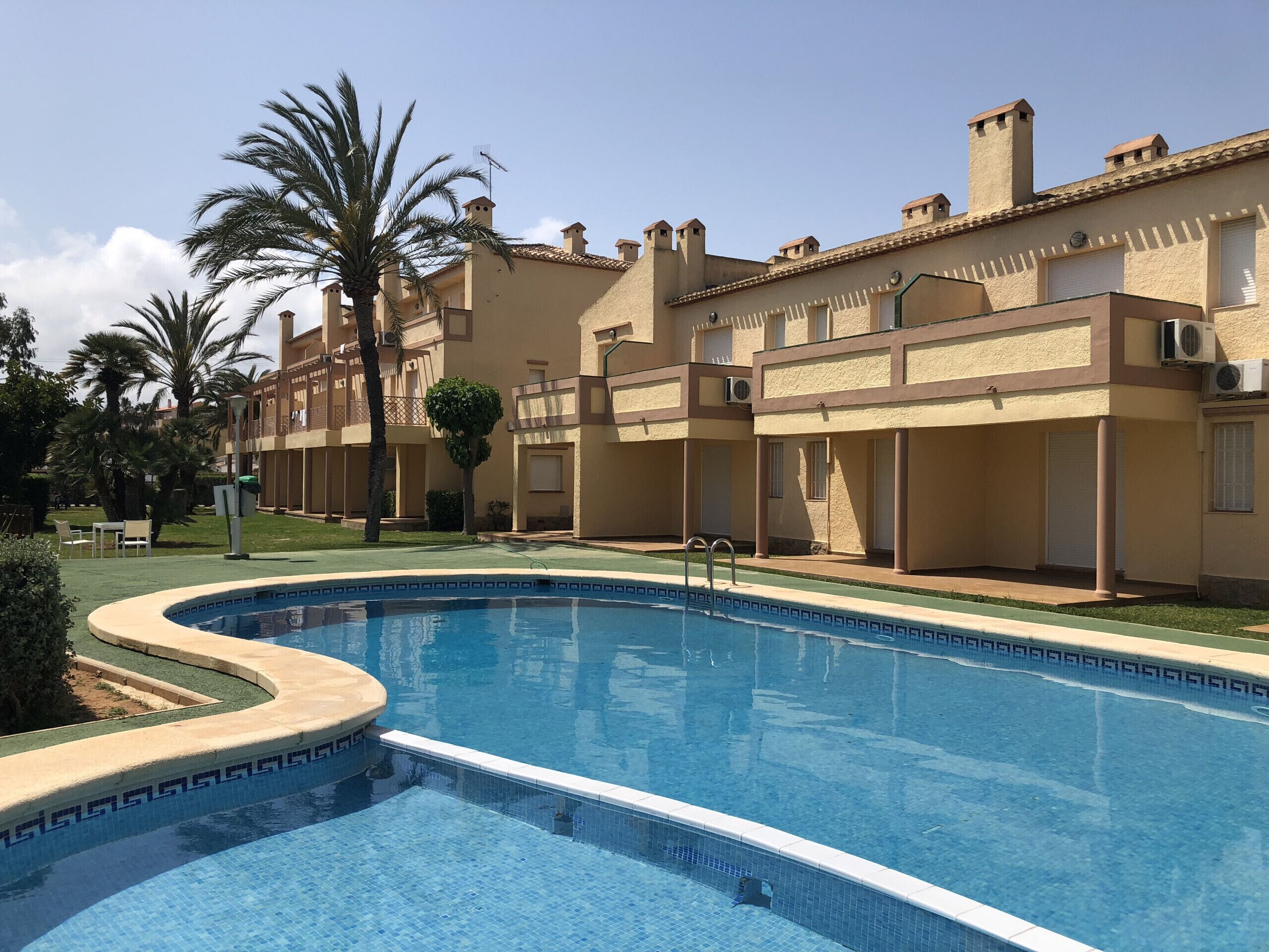 A swimming pool with a tiled edge, surrounded by a building with multiple balconies and air conditioning units.
