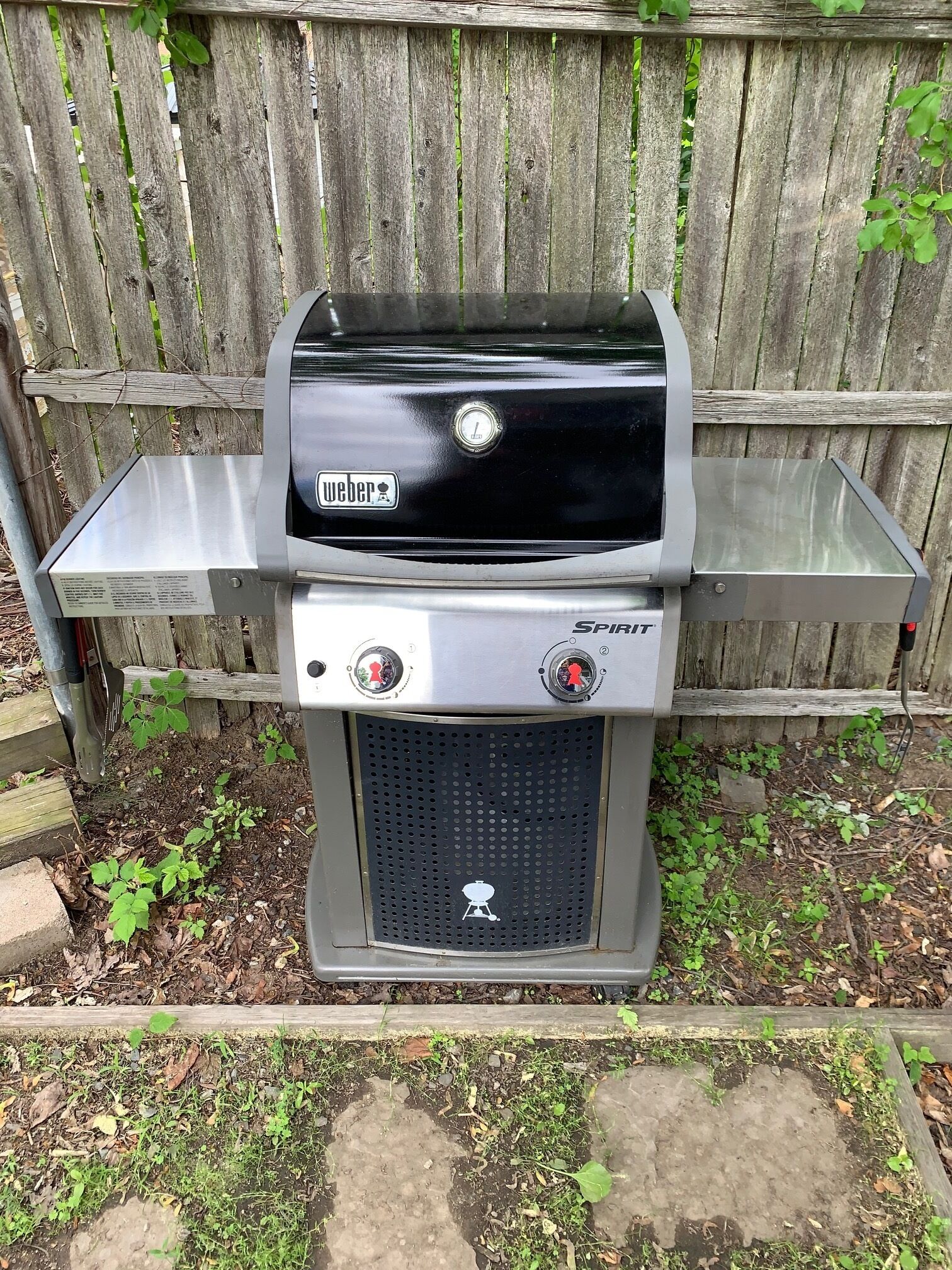 Ein Weber Spirit Holzkohlegrill mit Edelstahl-Bedienfeld, einer digitalen Uhr und einer Seitentisch.