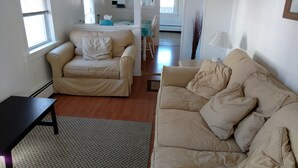 A living room with two beige sofas, a small black table, and a patterned rug. - 3 Bdr Vacation Rental - Walk To The Beach (Old Orchard Beach)