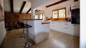 A modern kitchen with white cabinets, a wooden island with bar stools, and built-in appliances.