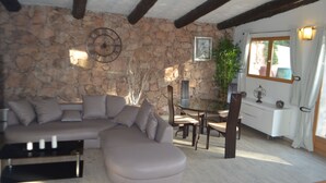 A living room with a stone wall, a sofa, a dining table with chairs, and a window with curtains.