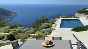 A poolside view with a table and chairs, a fruit bowl, and a view of the sea and mountains. - STUNNING LUXURY HOME WITH SEA, MOUNTAIN & SUNSET VIEWS. Private pool & terraces (Valldemossa, Mallorca)