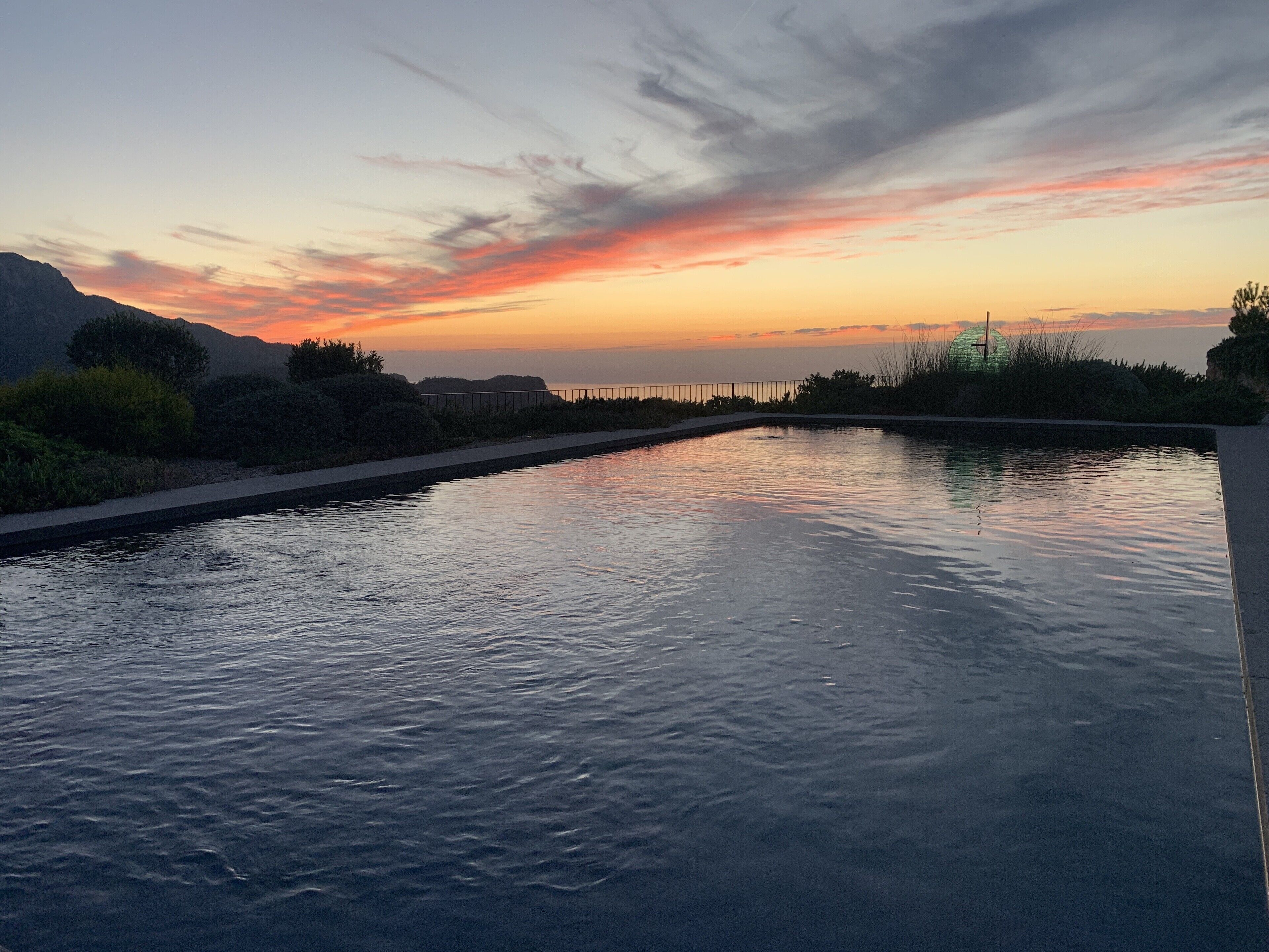 A swimming pool with a view of the sunset and mountains in the background.