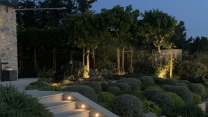 A well-lit outdoor staircase leading up to a stone building, surrounded by neatly trimmed bushes and trees. - STUNNING LUXURY HOME WITH SEA, MOUNTAIN & SUNSET VIEWS. Private pool & terraces (Valldemossa, Mallorca)