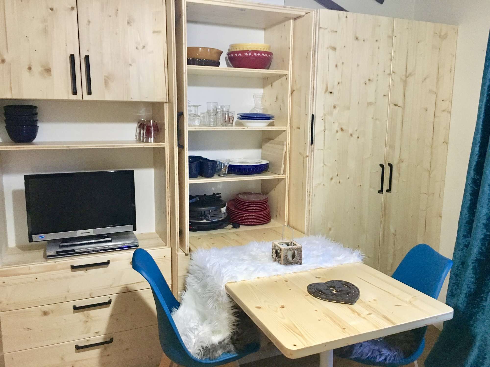 A compact room with a wooden cabinet, a television, a small table with a heart-shaped object, and a blue chair.