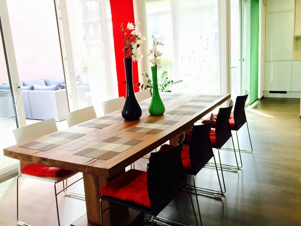 Un coin repas avec une table en bois, des chaises noires dotées de coussins rouges et deux vases ornés de fleurs.