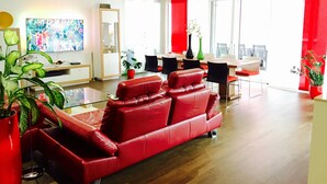 Un salon moderne avec un canapé rouge, un coin repas agrémenté de touches de rouge et de grandes fenêtres laissant entrer la lumière naturelle.